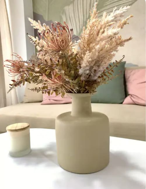 Arreglo de flores secas en jarrón de cerámica crema sobre mesa blanca en apartamento de Málaga, con cojines rosas en sofá de fondo