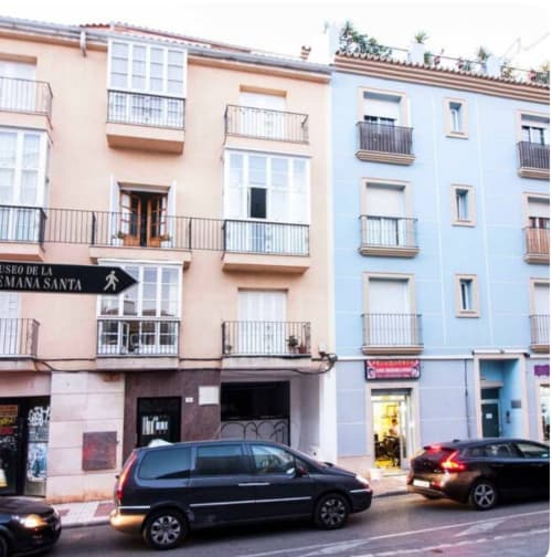 Colorido edificio histórico en Málaga Centro con balcones, tiendas en planta baja y coches aparcados en la calle