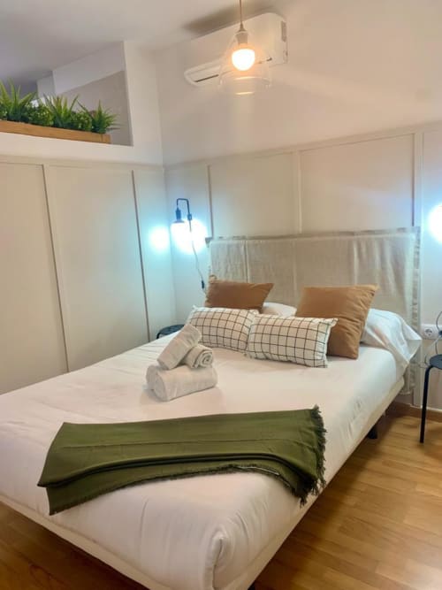 Dormitorio moderno en apartamento de Málaga Centro con cama queen, almohadas de cuadros, manta verde, iluminación colgante y aire acondicionado
