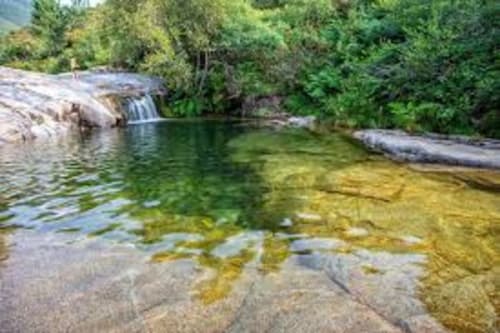 Poza de río cristalina con pequeña cascada rodeada de exuberante bosque verde en Aldea Rural Santo André, Ourense España
