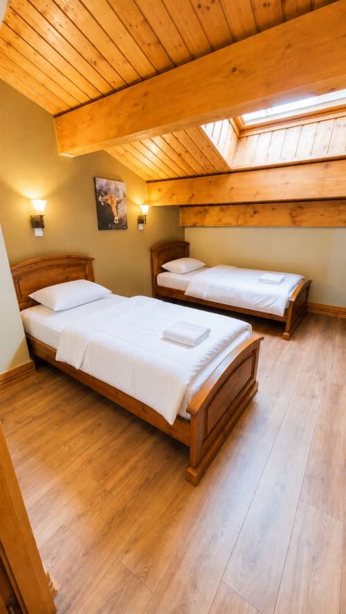 Chambre double avec lits en bois et poutres apparentes au Chalet des Cimes, hôtel en Savoie