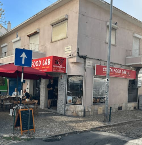 Fachada do restaurante Cousin Food Lab no albergue Vila Alexandra em Costa da Caparica, com toldo vermelho e assentos ao ar livre