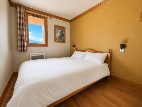 Chambre douillette au Chalet des Cimes avec mobilier en bois, literie blanche, murs jaune doré et vue sur les montagnes