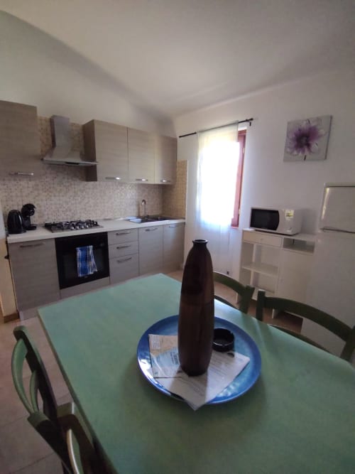 Modern kitchen and dining area in San Teodoro villa with gas stove, white cabinetry, and green table for guests