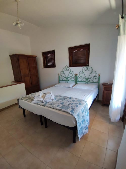 Spacious bedroom in San Teodoro villa with twin beds, wrought iron headboards, wooden furnishings, and garden views through
