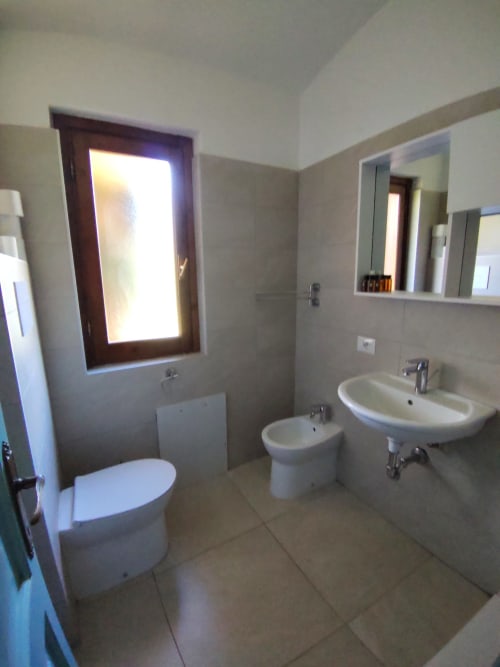 Modern bathroom in Oasi Villetta Standard villa at Holidays San Teodoro with dual sinks, toilet, and window with garden views