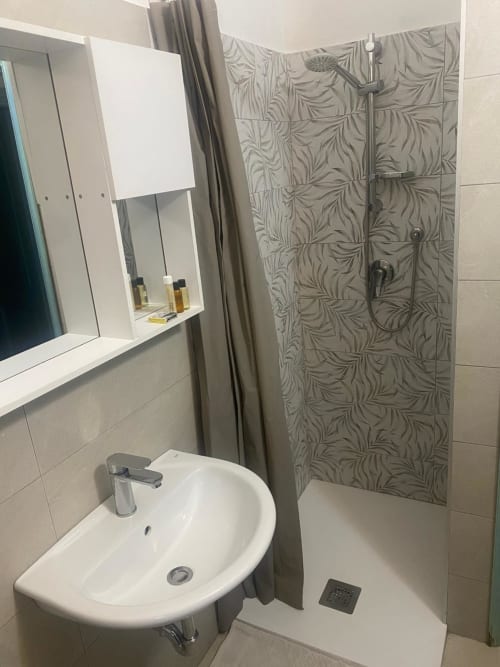 Modern bathroom with white sink, mirror cabinet, and walk-in shower with leaf-patterned tiles at Holidays San Teodoro villa,