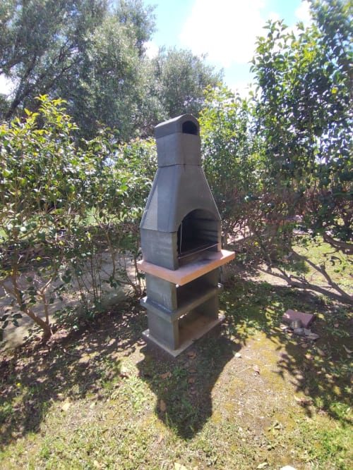 Outdoor stone fireplace in lush garden at Holidays San Teodoro villa with green vegetation surrounding