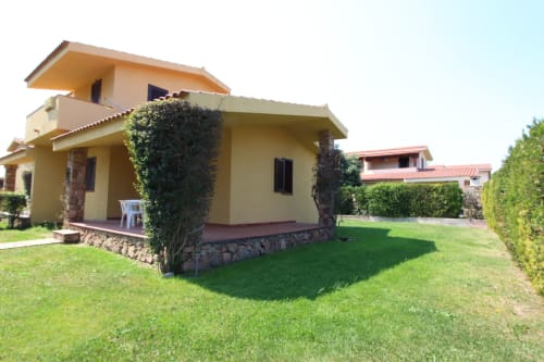 Yellow villa with stone foundation, green lawn, and ivy at Holidays San Teodoro, San Teodoro