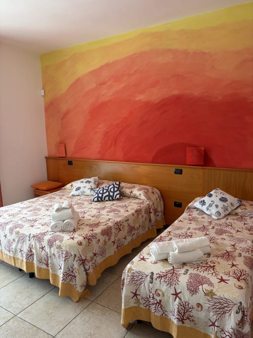 Camera luminosa di Villa Arneide con due letti, biancheria a tema marino, testata in legno e murale tramonto vibrante
