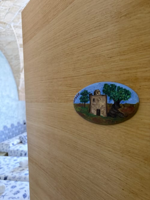 Pietra decorativa dipinta a mano con torre medievale e ulivi su muro in legno a Villa Arneide