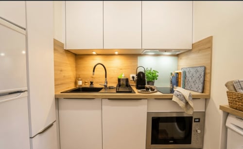 Petite cuisine moderne avec armoires blanches, dosseret en bois, évier noir, micro-ondes et cafetière à Conciergerie IB