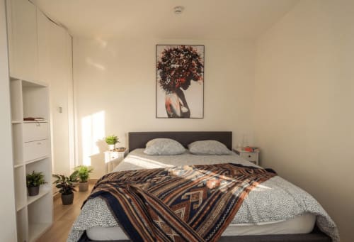 Chambre moderne avec lit queen-size, oreillers gris, plaid à motifs, étagères blanches, plantes et tableau portrait à Conciergerie IB
