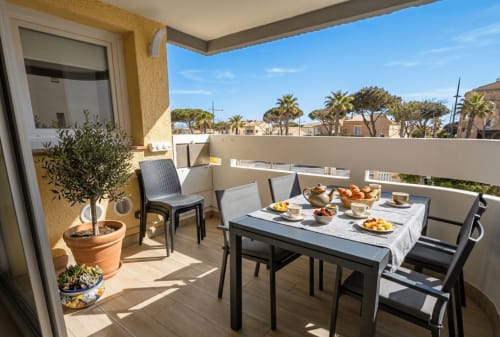 Terrasse ensoleillée de la Conciergerie IB à Canet-en-Roussillon avec table à manger, chaises, plantes en pots et vue sur la Méditerranée