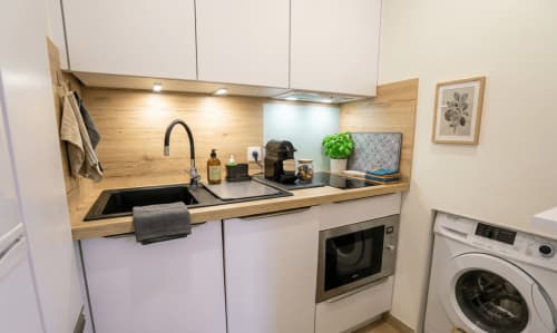 Cuisine moderne avec armoires blanches, comptoir en bois, évier noir et appareils en acier inoxydable à la Conciergerie IB