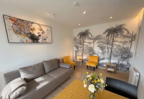 Salon moderne à Conciergerie IB, Canet-en-Roussillon, avec canapé gris, accents jaunes et fresque murale tropicale