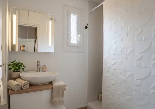 Salle de bain moderne à la Conciergerie IB à Canet-en-Roussillon avec vasque ronde, carrelage blanc texturé et miroir intégré