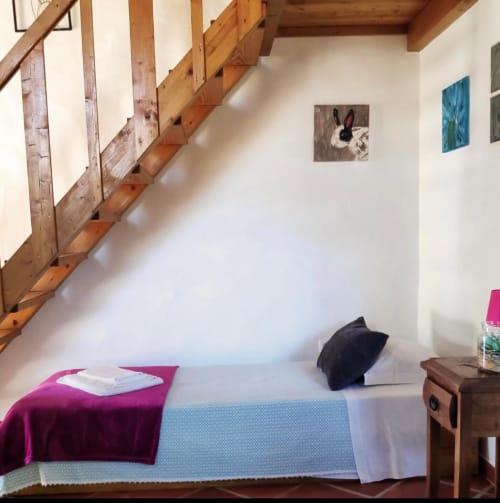 Gemütliches Schlafzimmer im T Monte Porto Côvo mit Holztreppe, Bett mit magentafarbener Decke und gerahmten Kunstwerken an weißen Wänden