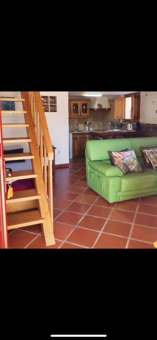 Área de estar clara com sofá verde, escadas de madeira e cozinha equipada no T Monte BnB em Porto Côvo