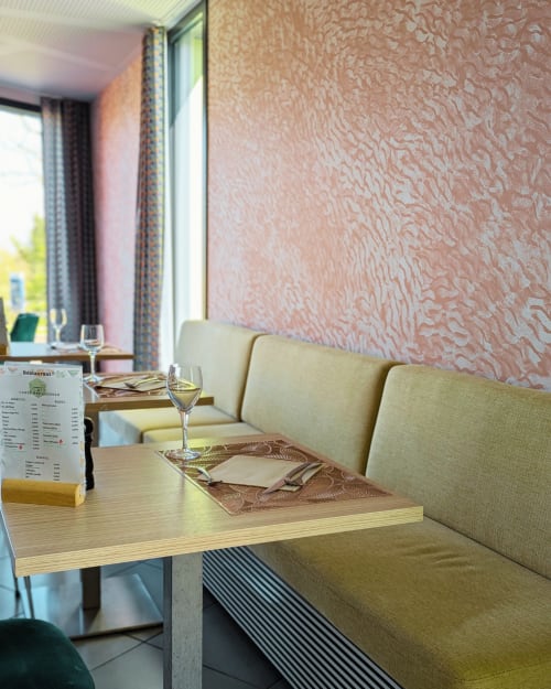 Coin repas de l'hôtel La Verriaire avec banquette crème, table en bois et mur rose corail texturé à Chanverrie