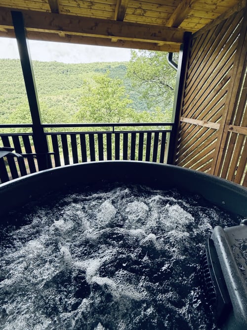 Bain à remous bouillonnant sur la terrasse du lodge avec vue sur la vallée forestière de montagne aux Cabanes et lodges du Belvédère, Serrières-sur-Ain