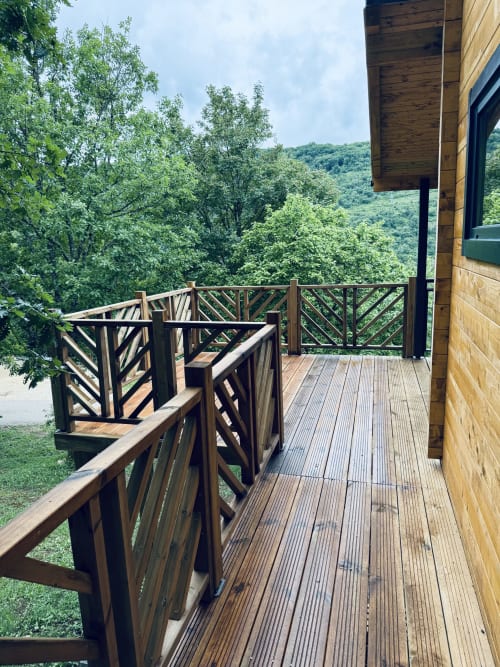 Wooden terrace with geometric railings overlooking forested valley at Cabanes et lodges du Belvédère, Serrières-sur-Ain