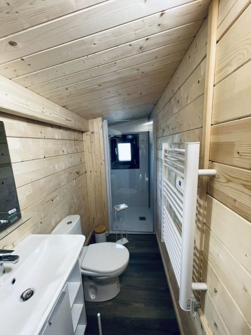 Modern wooden bathroom with white sink, toilet, and shower in Lodge Hibiscus villa at Cabanes et lodges du Belvédère,