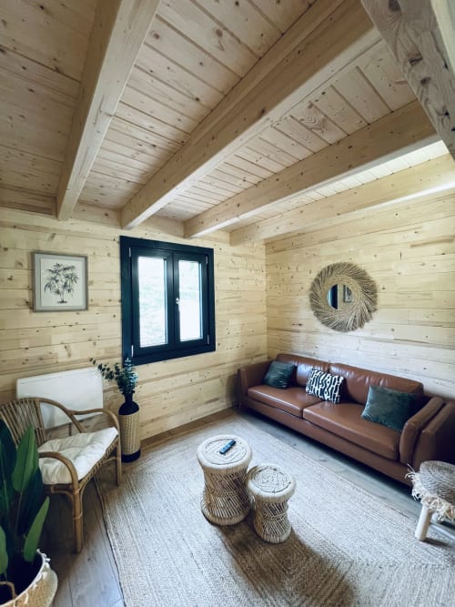 Modern wooden lodge interior with brown leather sofa, rattan chair, and exposed beam ceiling at Cabanes et lodges du
