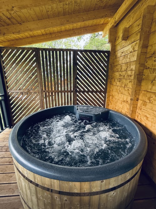 Hot tub with ash-filled basin on wooden deck under covered pergola at Cabanes et lodges du Belvédère, Serrières-sur-Ain