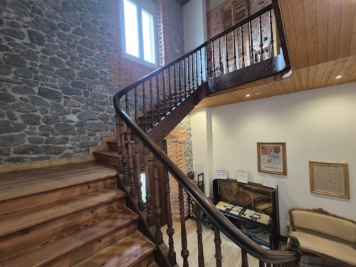 Spiral wooden staircase with dark railing in Fabrica de Atardeceres apartment, stone walls and modern lighting visible.