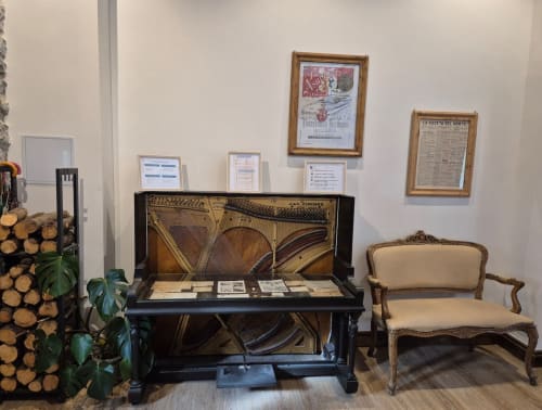Room 3-Juan Pinto at Fabrica de Atardeceres showing a vintage piano, upholstered chair, framed artwork, and decorative