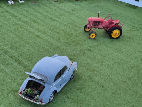Tractor rosa vintage y auto clásico azul celeste en pasto verde en Fabrica de Atardeceres, escenario del campo español