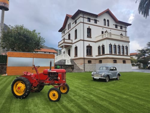 Tractor rojo vintage y automóvil clásico en el jardín del hotel Fabrica de Atardeceres con mansión colonial en España