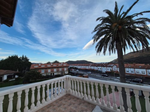 Vista desde el balcón de Fabrica de Atardeceres con palmera, edificios del pueblo y colinas bajo cielo azul