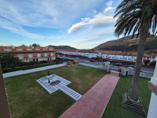 Patio de Fabrica de Atardeceres con jardín verde, palmera, camino rojo y zona de estacionamiento con cargador eléctrico en España