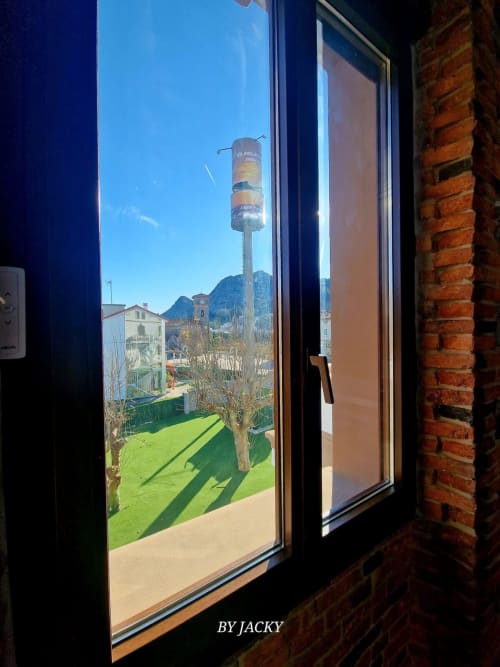 Vista desde la ventana mostrando césped verde, montañas al fondo y edificios del pueblo del apartahotel Fábrica de Atardeceres en España