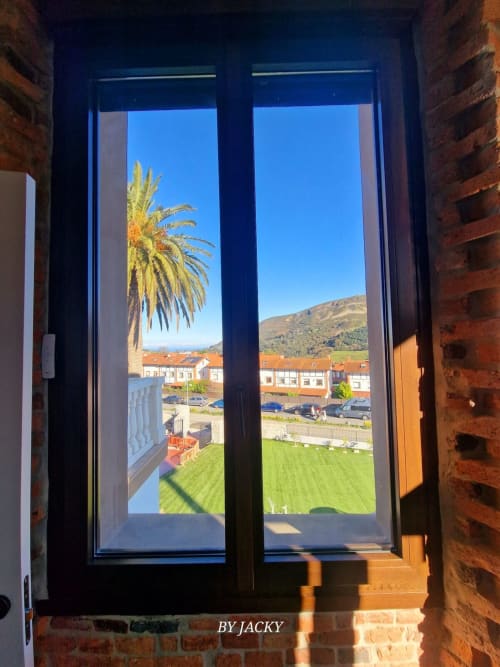 Vista desde el apartamento Fabrica de Atardeceres mostrando palmera, ladera, estacionamiento y edificios bajo cielo azul