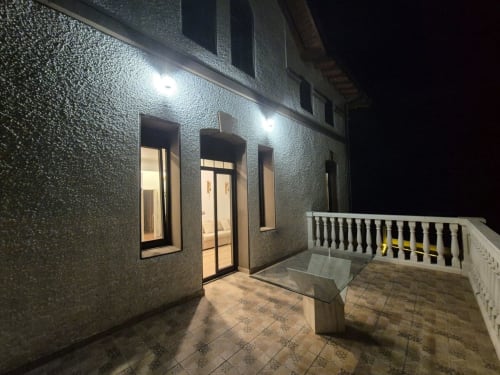 Fachada iluminada del apartamento Fabrica de Atardeceres de noche, con puertas de entrada y barandilla blanca del balcón