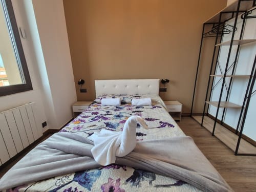 Modern bedroom at Fabrica de Atardeceres hotel in Spain with white headboard bed, purple floral bedding, wooden floor, and