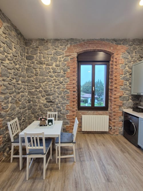 Modern kitchen-dining area with stone walls, white dining table, and dark window at Fabrica de Atardeceres, Spain