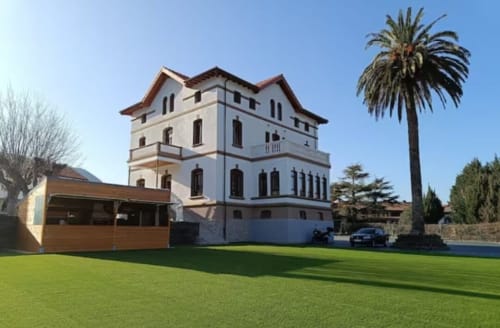 Fabrica de Atardeceres hotel exterior in Spain with white mansion, manicured lawn, palm tree and modern wooden structure