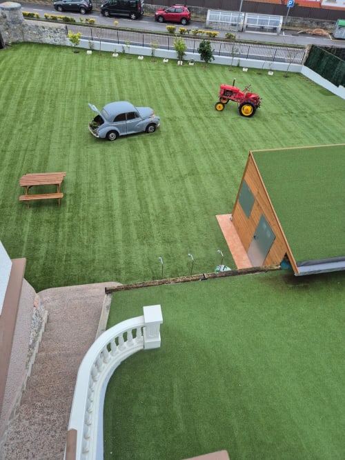 Fabrica de Atardeceres courtyard with miniature car and tractor on green grass, wooden bench and structures