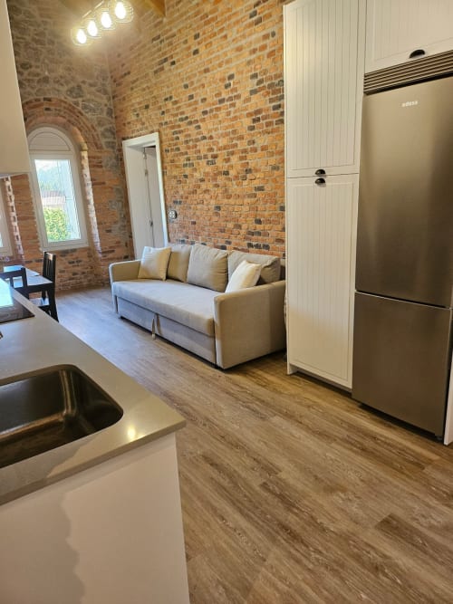 Modern open-plan apartment at Fabrica de Atardeceres showing kitchen, living area with beige sofa, exposed brick walls, and