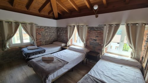 Spacious bedroom at Fabrica de Atardeceres with multiple beds, exposed brick walls, wooden beams, and large windows with