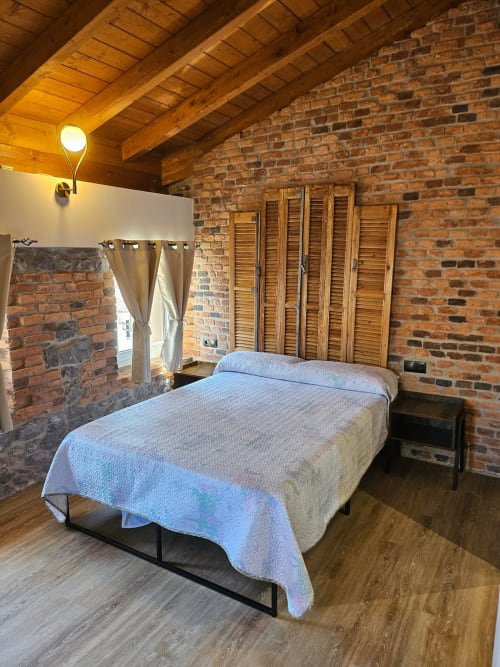 Rustic apartment bedroom at Fabrica de Atardeceres with brick walls, wooden beams, queen bed, and wooden louvered closet