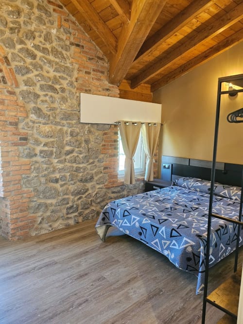 Rustic bedroom at Fabrica de Atardeceres with exposed stone walls, wooden beams, and blue patterned bed