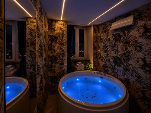 Salle de bain spa luxe à HomeholidaySanremo avec jacuzzi bleu illuminé, papier peint tropical et vue sur la mer de Sanremo
