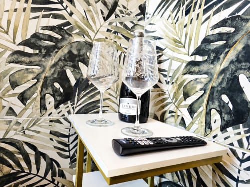 Élégant studio à HomeHolidaySanremo avec bouteille de vin, verres et télécommande sur table blanche devant feuillages tropicaux