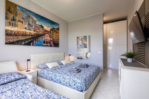 Modern bedroom with blue patterned bedding, Venice canal artwork, white wardrobe, and city view in Milano apartment