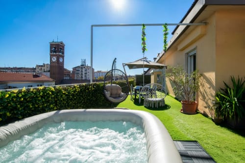 Luxury Milano apartment terrace with private hot tub, hanging chair, and city view of historic bell tower